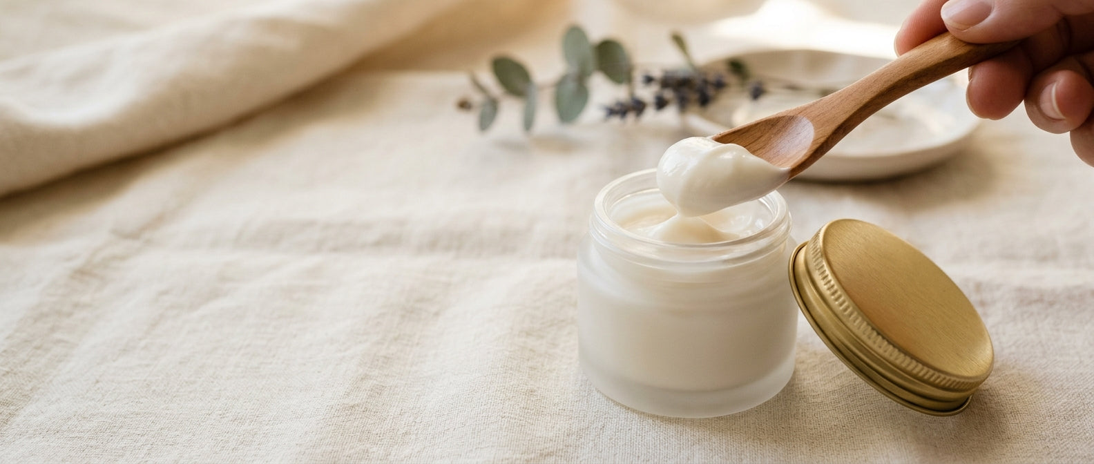 Wooden spatula scooping pearl cream from frosted jar — moisturize