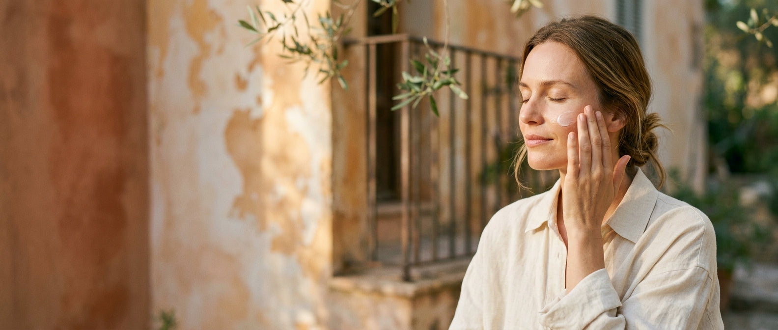 Woman applying sunscreen on cheek in warm Mediterranean light — protect