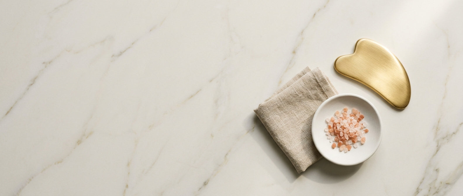 Cream marble flat-lay with gua-sha tool and pink salt — texture and dullness